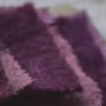 Huit coupons de laine mordancés à la betterave et de différentes nuances de violet posés sur une planche de bois